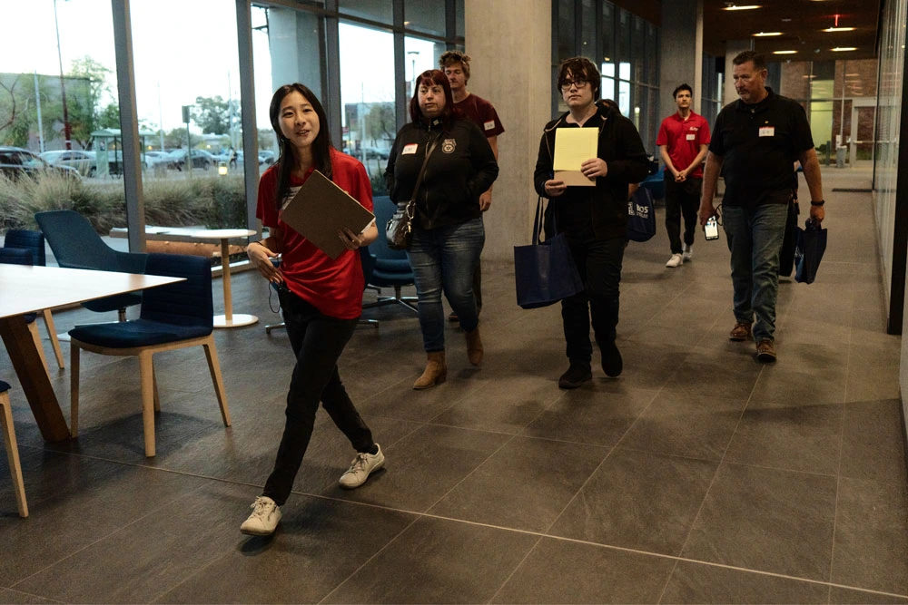 Group of five individuals walking through a modern lobby, carrying notebooks and wearing lanyards.