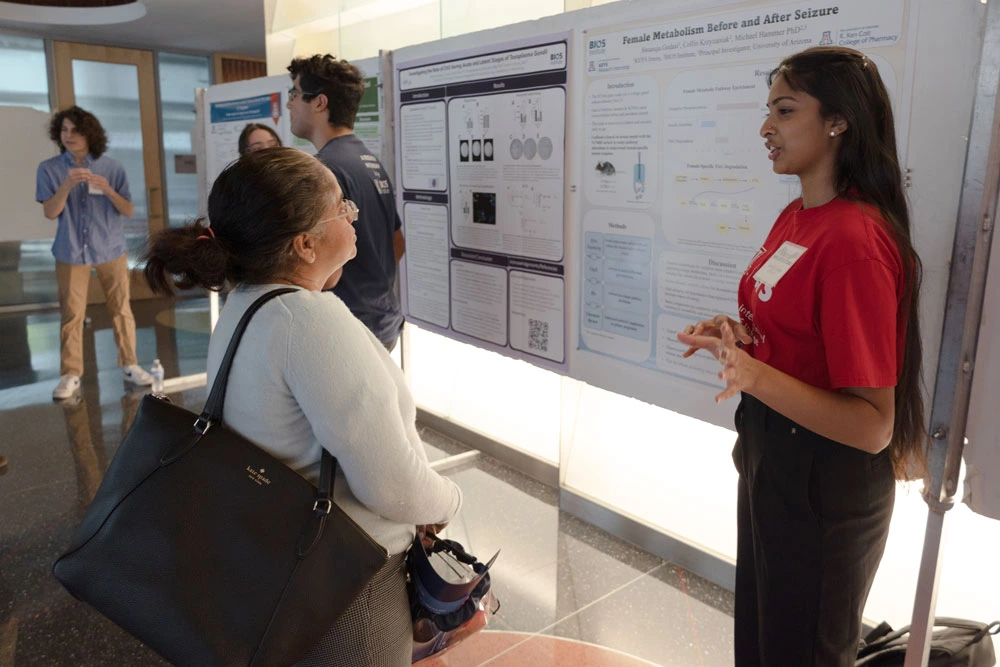 Two individuals discussing a scientific poster presentation at an event. Other attendees are visible in the background.