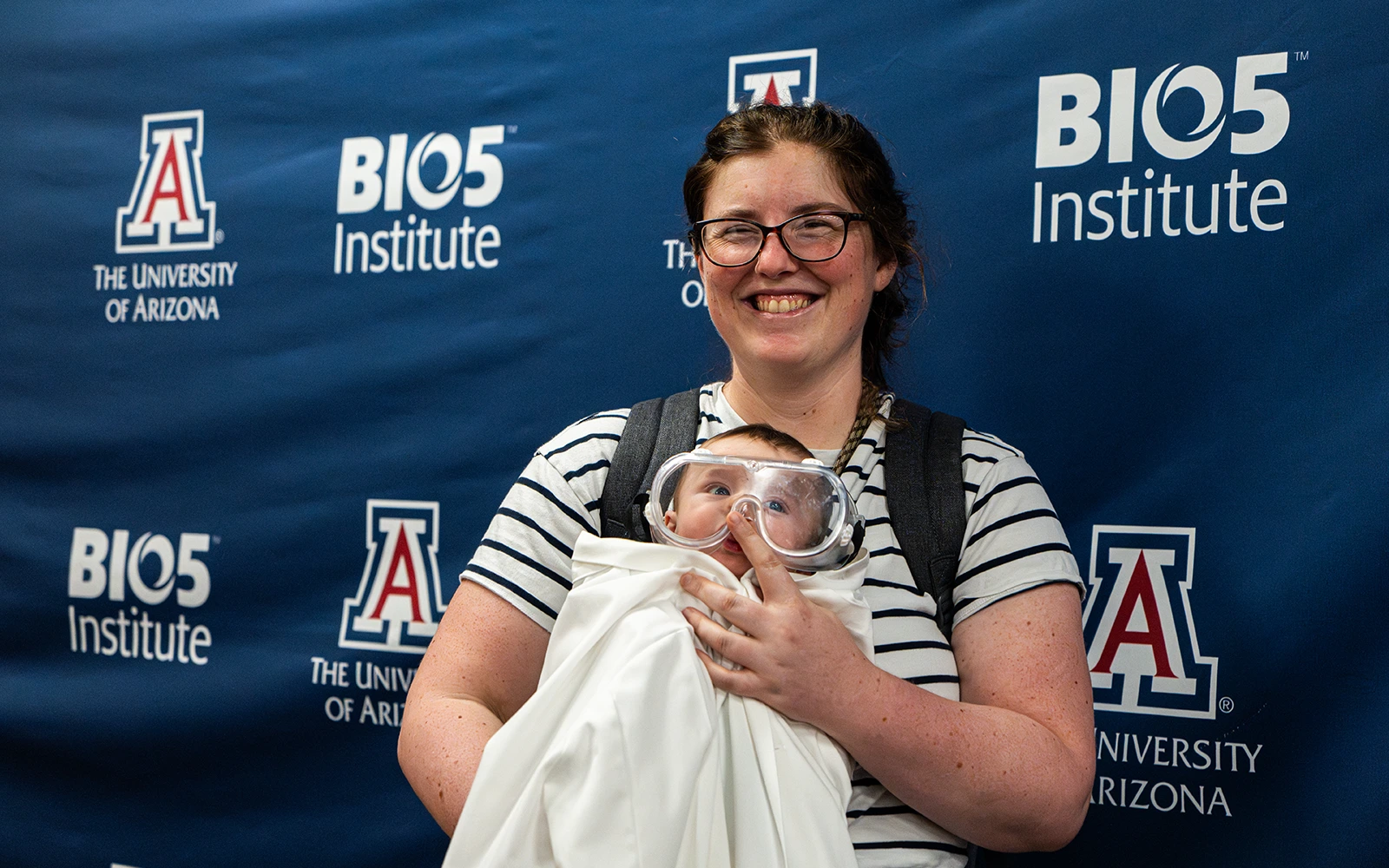 A mother with her baby who is dressed in a lab coat and safety goggles