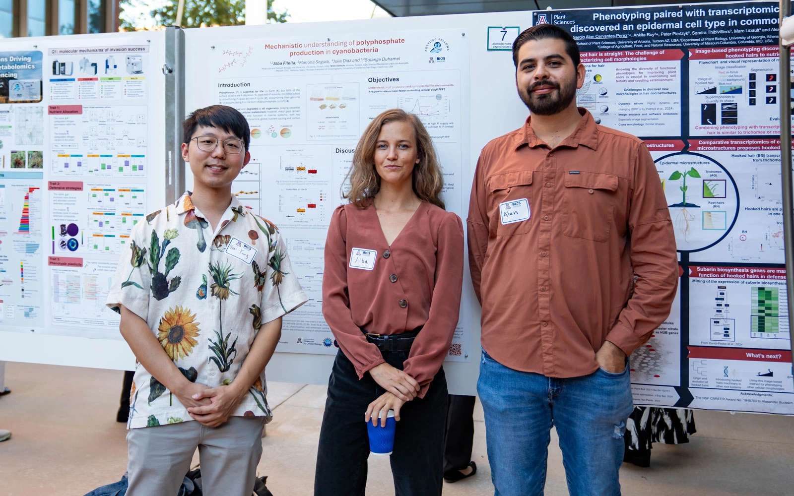 Three professionals standing in front of scientific posters at a conference, each wearing a name badge.