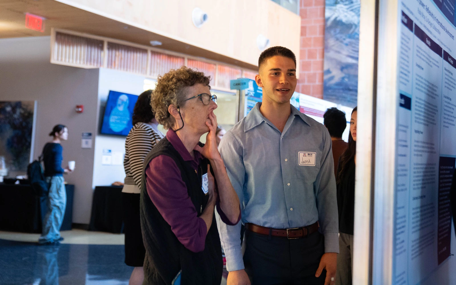 Two individuals engage in a discussion beside a poster presentation at a professional conference.