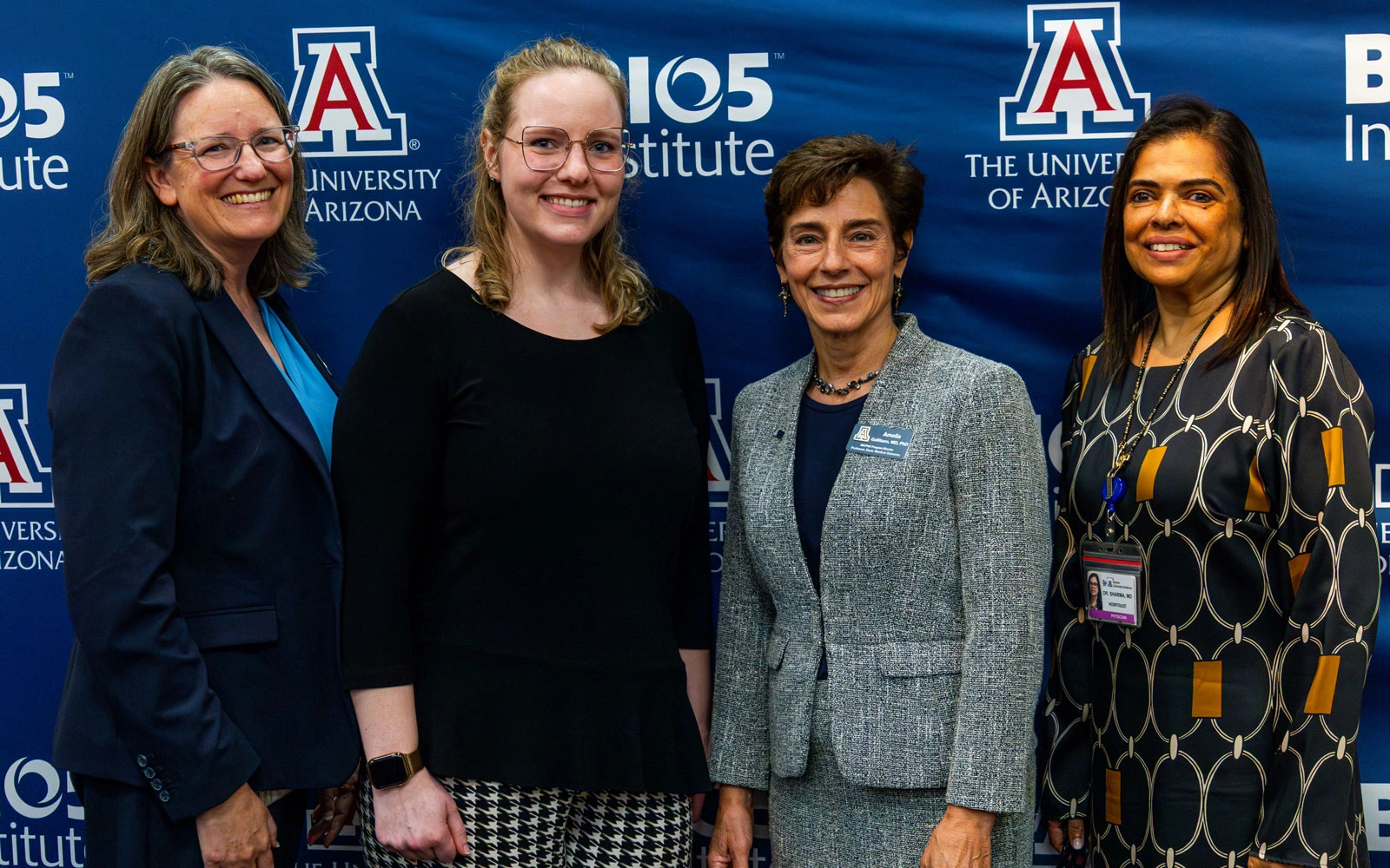 Four individuals posing at an event with banners for the University of Arizona and BIO5 Institute in the background.