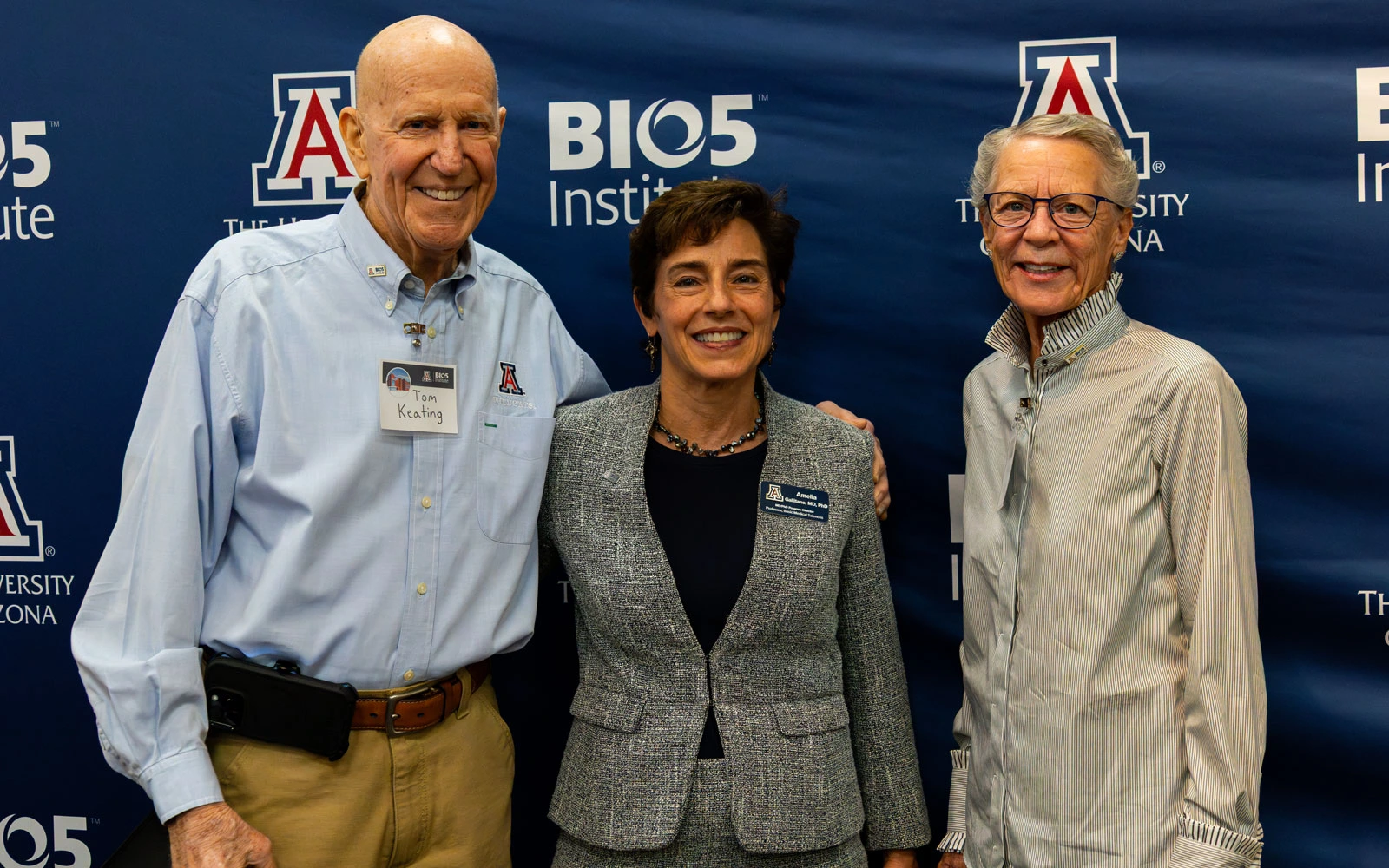 Three individuals standing together and smiling at a University of Arizona BIO5 Institute event, with banners of the institute and university visible in the background.