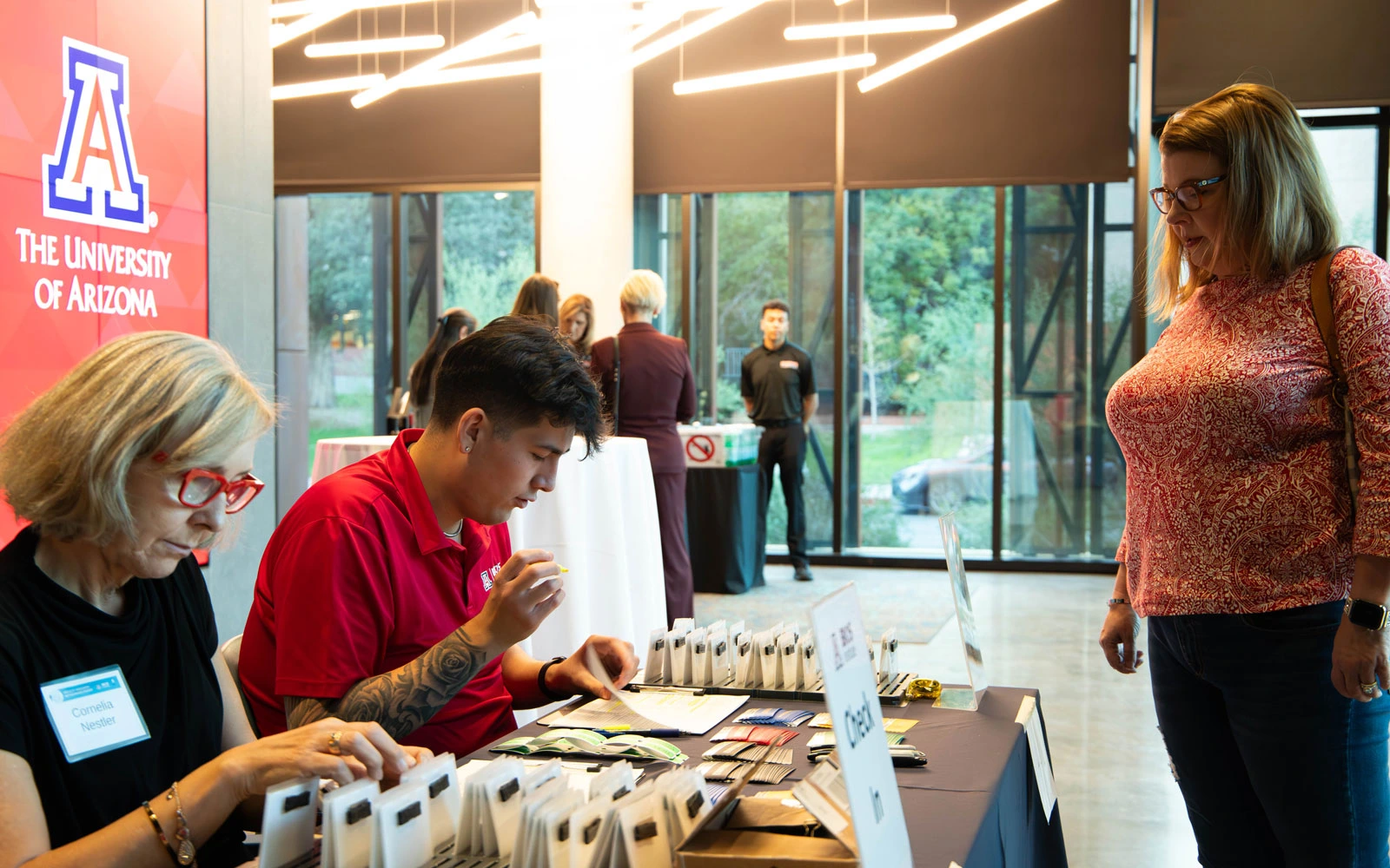 Individuals checking in people at a University of Arizona event booth indoors, with others in the background.