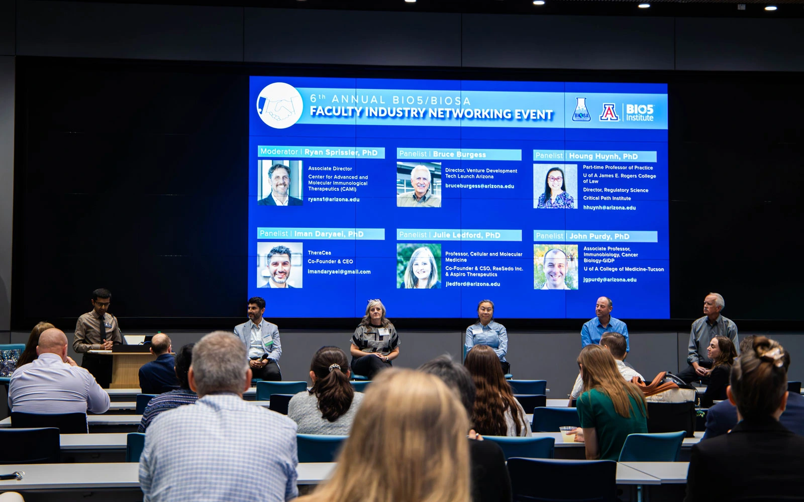 Participants at the 6th Annual BIO5/BIOSA Faculty Industry Networking Event sitting on panel in front of audience with event details and speaker names displayed on screen behind them.