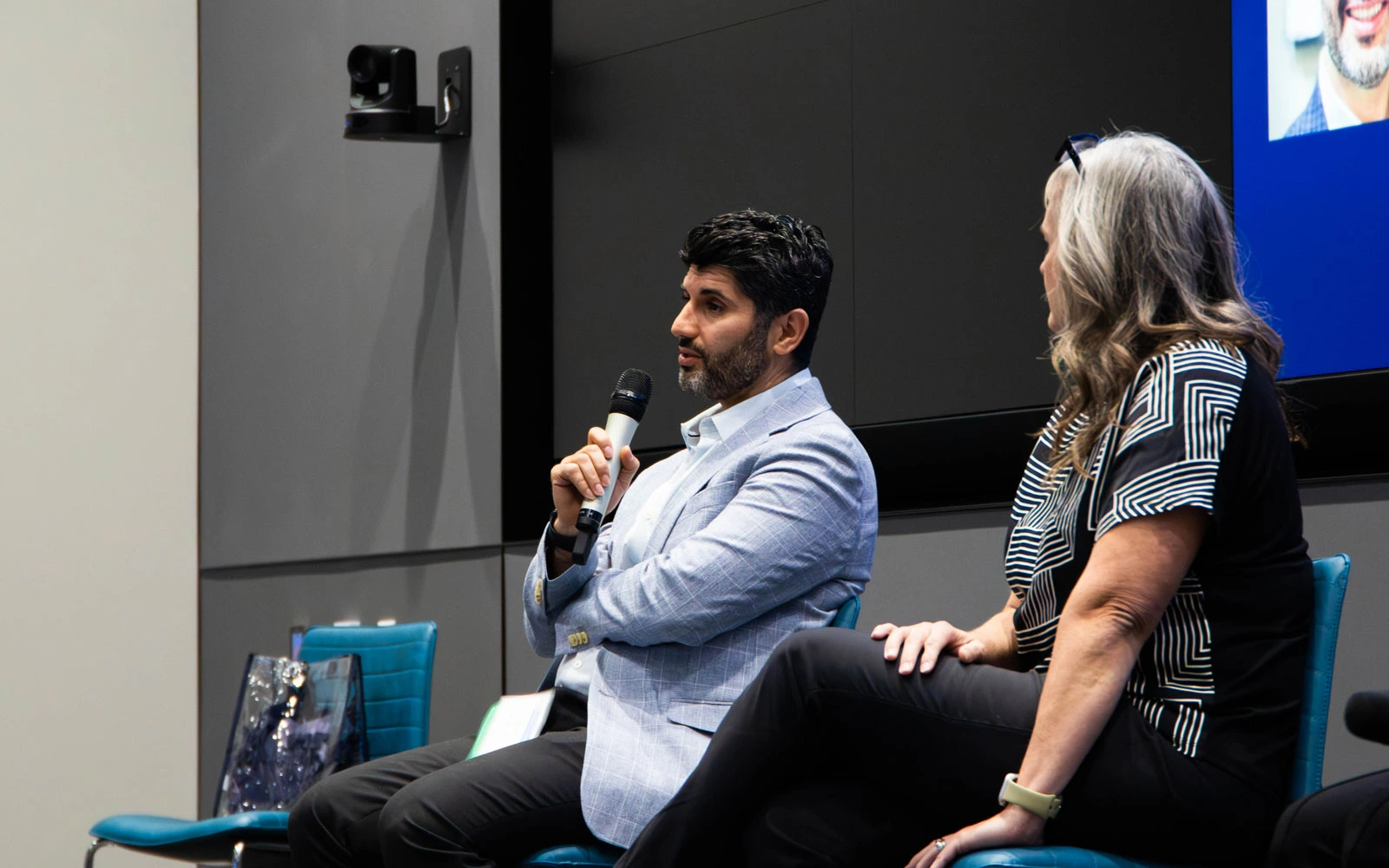 Two individuals sitting on a stage participating in a discussion, one holding a microphone.