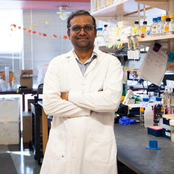 Person in a white lab coat with crossed arms standing in a lab setting