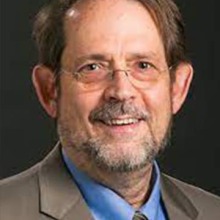 Headshot of Dr. Alfred Bothwell wearing a brown suit jacket against a black background