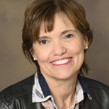 Headshot of Dr. Maria Altbach wearing a dark  clothes against a brown background