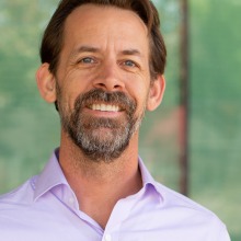 Headshot of Dr. Jeff Oliver wearing a lavendar shirt against a green background