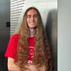 Young man with long hair wearing a red shirt stands confidently with his arms crossed