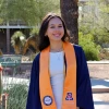 A person wearing a University of Arizona engineering graduation stole stands smiling outdoors in a sunny campus setting.