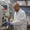 A scientist wearing a lab coat and gloves is working with samples in a centrifuge in a well-equipped laboratory.