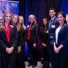 Group of seven individuals standing with confident smiles at a University of Arizona BIOS Institute recruitment booth, where banners and promotional materials are visible in the background.