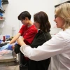 Three individuals work on a scientific experiment in a laboratory setting, using a laptop and lab equipment.