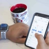 Person checking health statistics on a smartphone with health monitoring app, with an Apple Watch on their wrist and a coffee mug nearby.