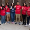 Group of six smiling students in red KEYS t-shirts pointing towards the camera, standing outdoors.