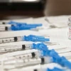 Syringes and a vial labeled 'COVID-19 Vaccine' arranged on a table.