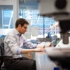 A person wearing glasses is working at a laptop in a modern laboratory, surrounded by scientific equipment.