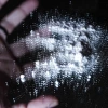 A hand releasing a puff of fine powder against a dark background.