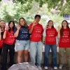 Group of eight students wearing KEYS program t-shirts, smiling and making a 'peace' hand sign outdoors on a sunny day.