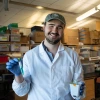 Man in lab gear holding a plant and green vial