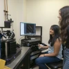 Two people in a laboratory setting are engaged with microscopy equipment on a desk. 