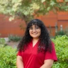 Person in a red shirt and dark curly hair against a green backdrop