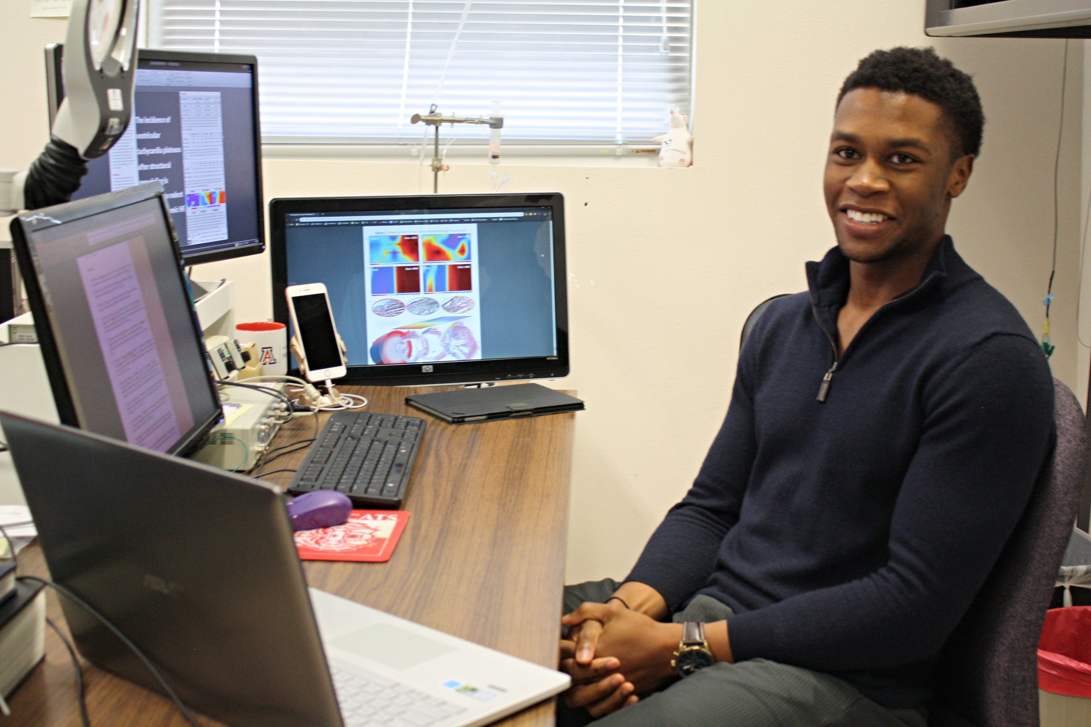 MD/phD student Ike Chinyere in his office, surrounded by four screens at a desk. 