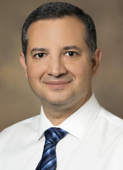 Headshot of Dr. Paulo Pires wearing a white shirt against a brown background