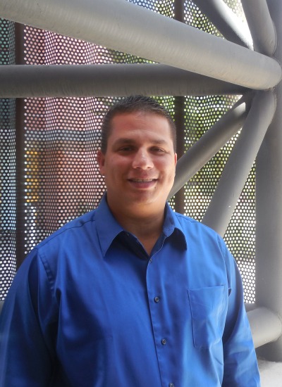 Robert Sandoval wearing a blue shirt against a gray geometric background
